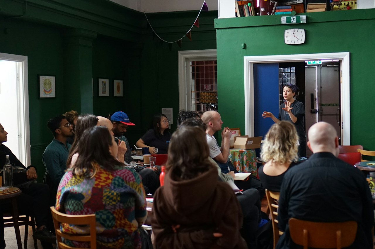 a diverse group of people sit listening to a woman talk.