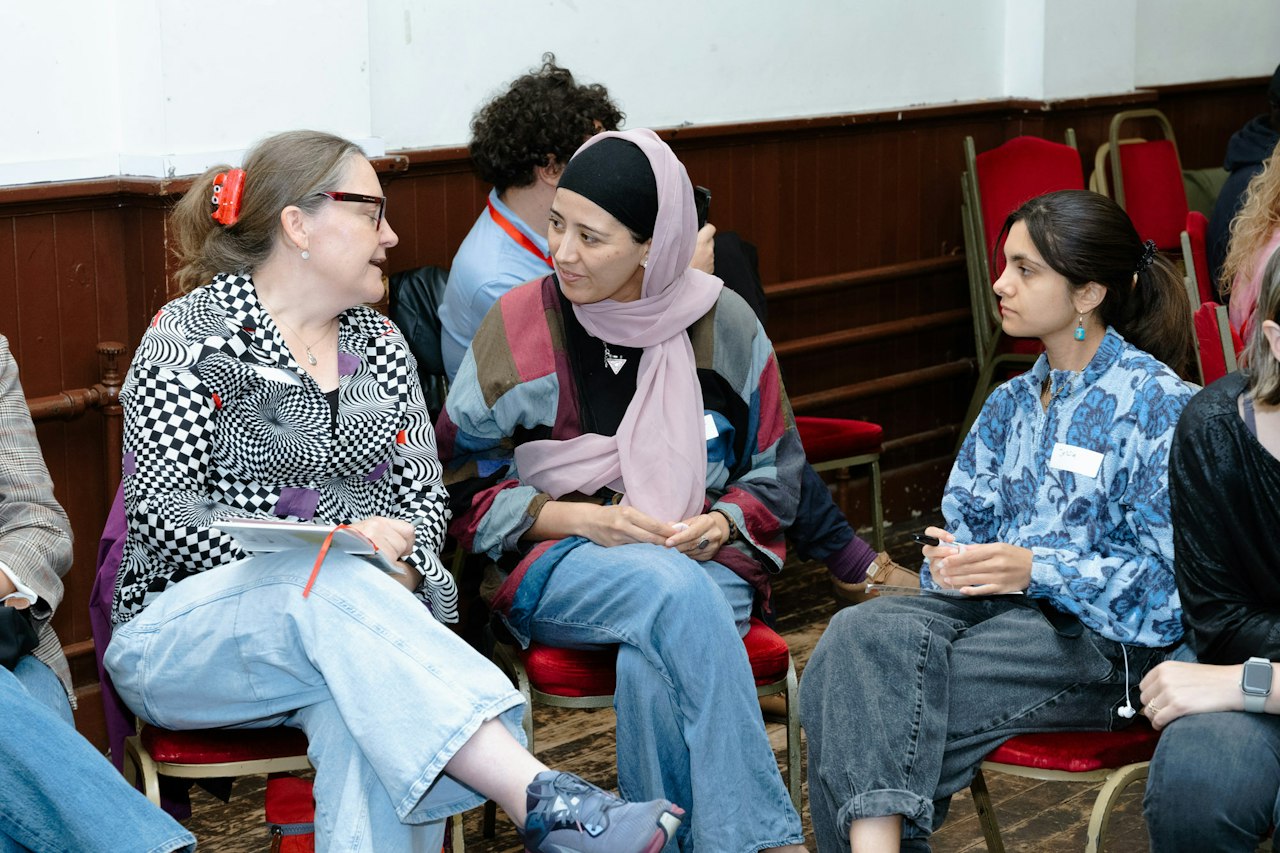 Three people sit on chairs and chat at an event, looking intently at each other.